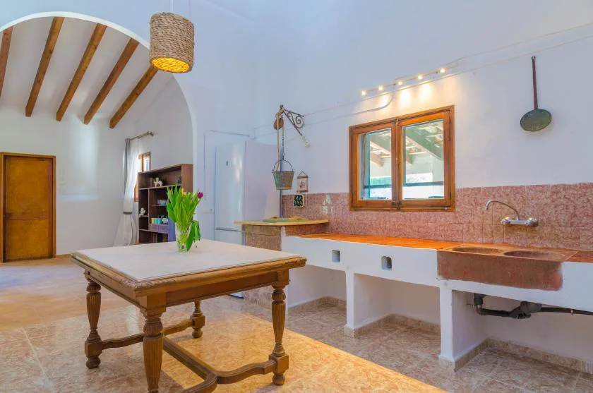 A spacious kitchen with a central wooden table and a long counter beneath a window.