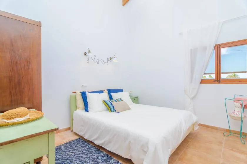 A bright bedroom with a bed, colorful pillows, and a window.