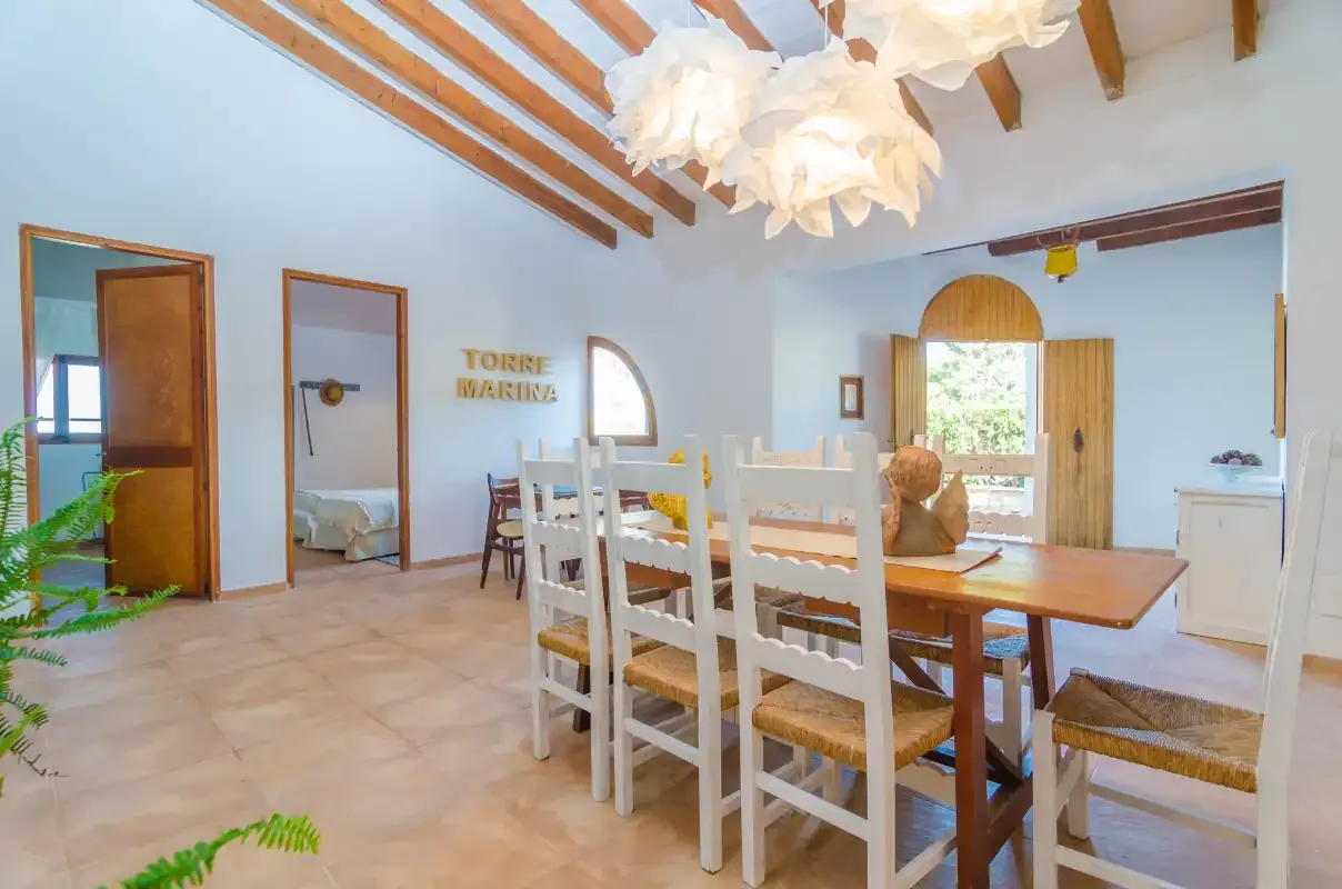 A bright dining area with a wooden table and white chairs beneath exposed ceiling beams.