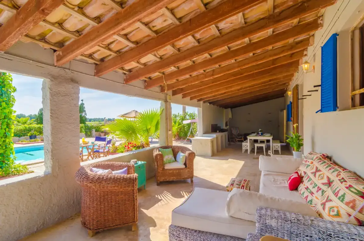 A covered patio has outdoor seating and views of a garden and pool.