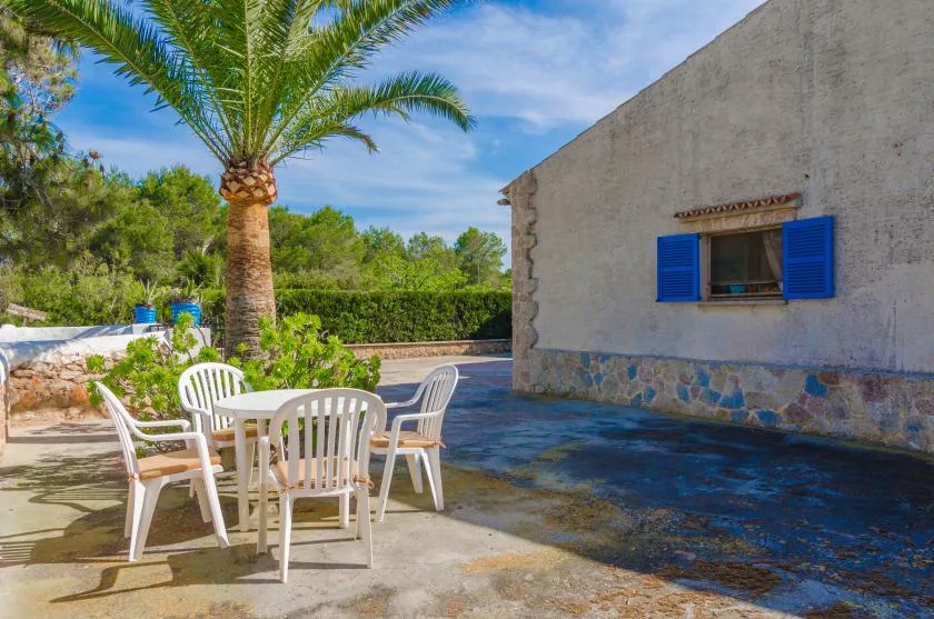 An outdoor patio with white seating beside a stone-faced building and palm tree.