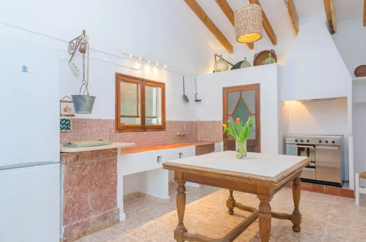 A bright kitchen with a central wooden table and exposed ceiling beams.