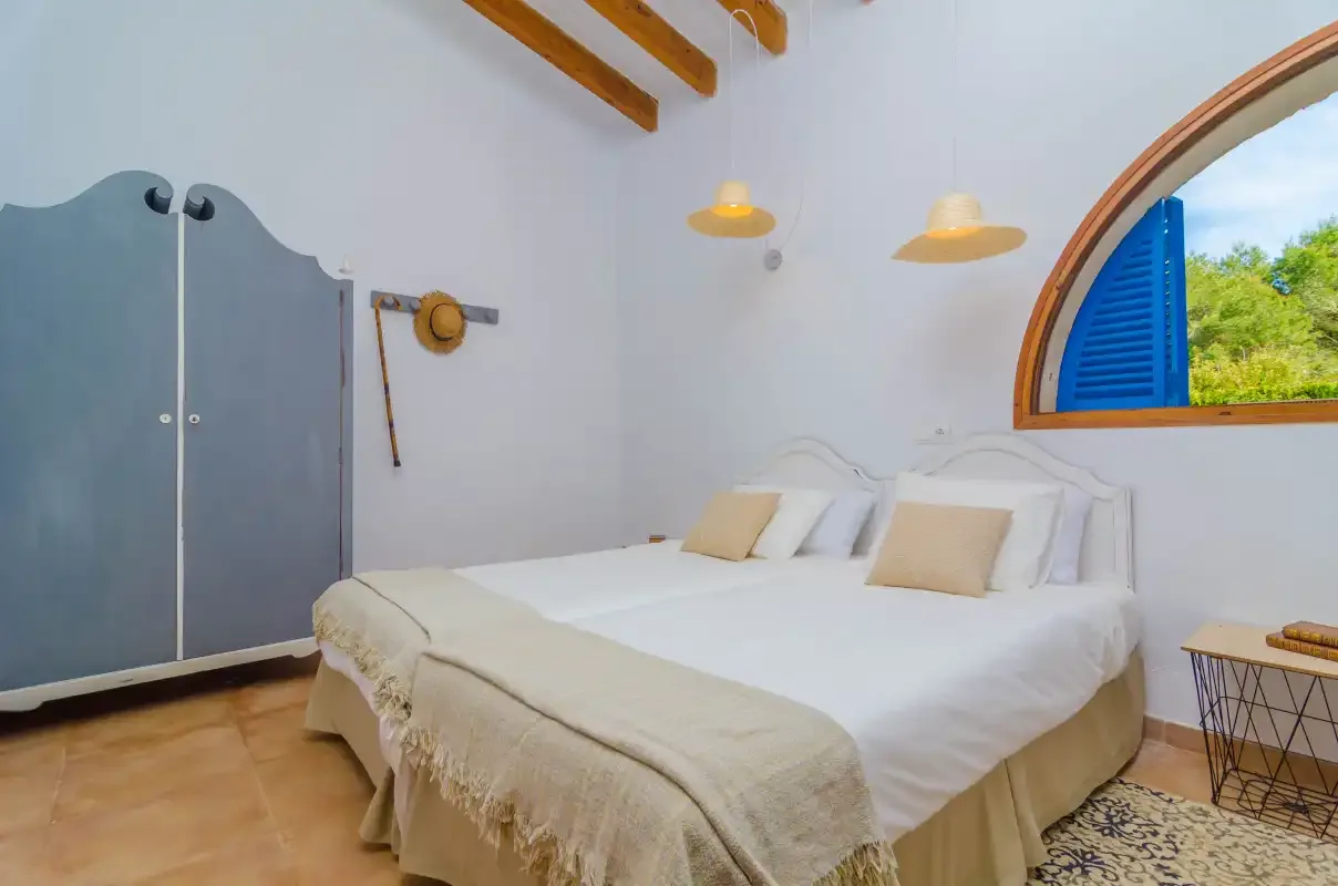 A bedroom with a double bed and an arched window with blue shutters.