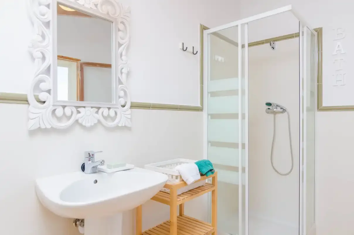 A bright bathroom with a sink, ornate mirror, and shower.