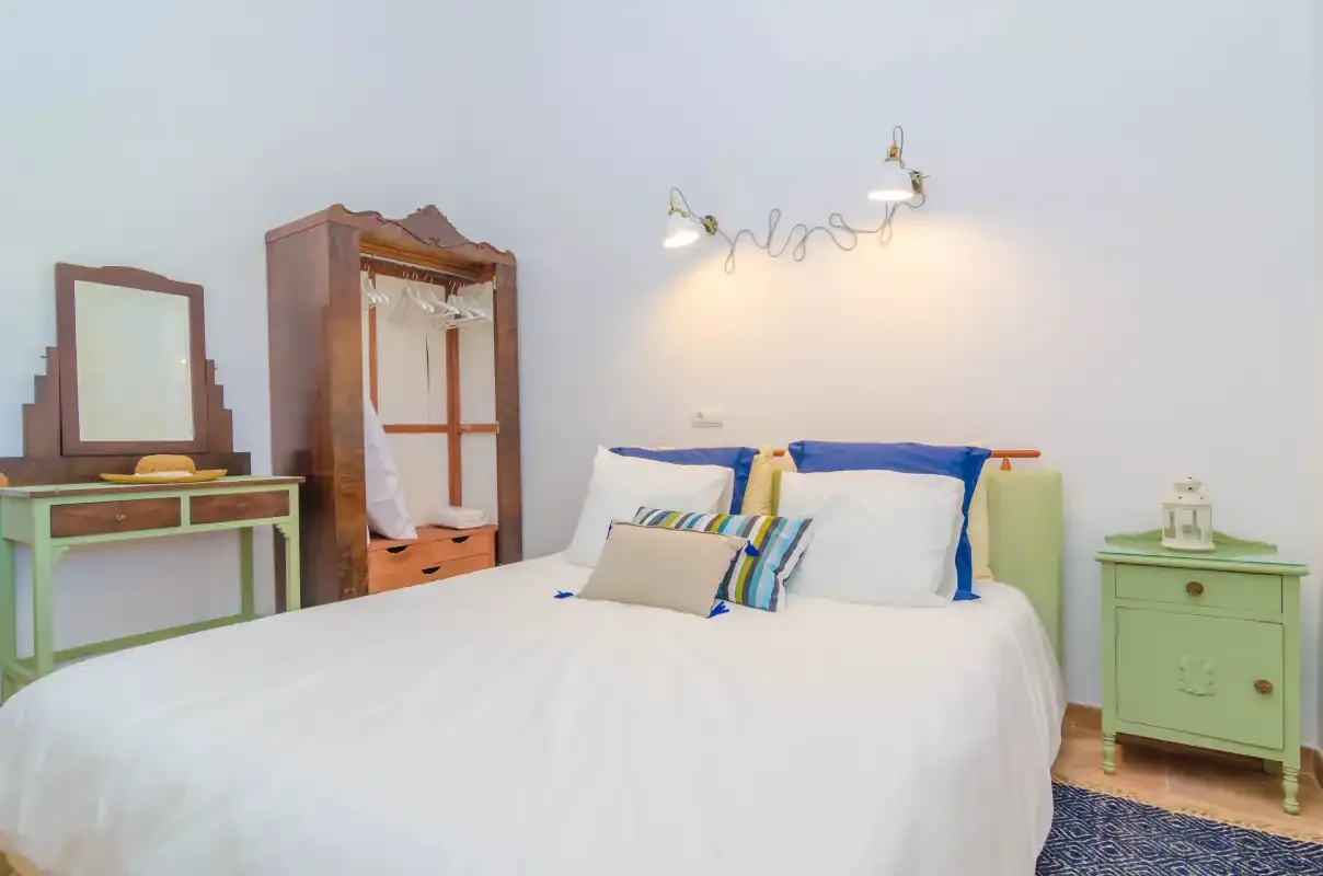 A bedroom with a white bed, colorful pillows, and green bedside furniture.
