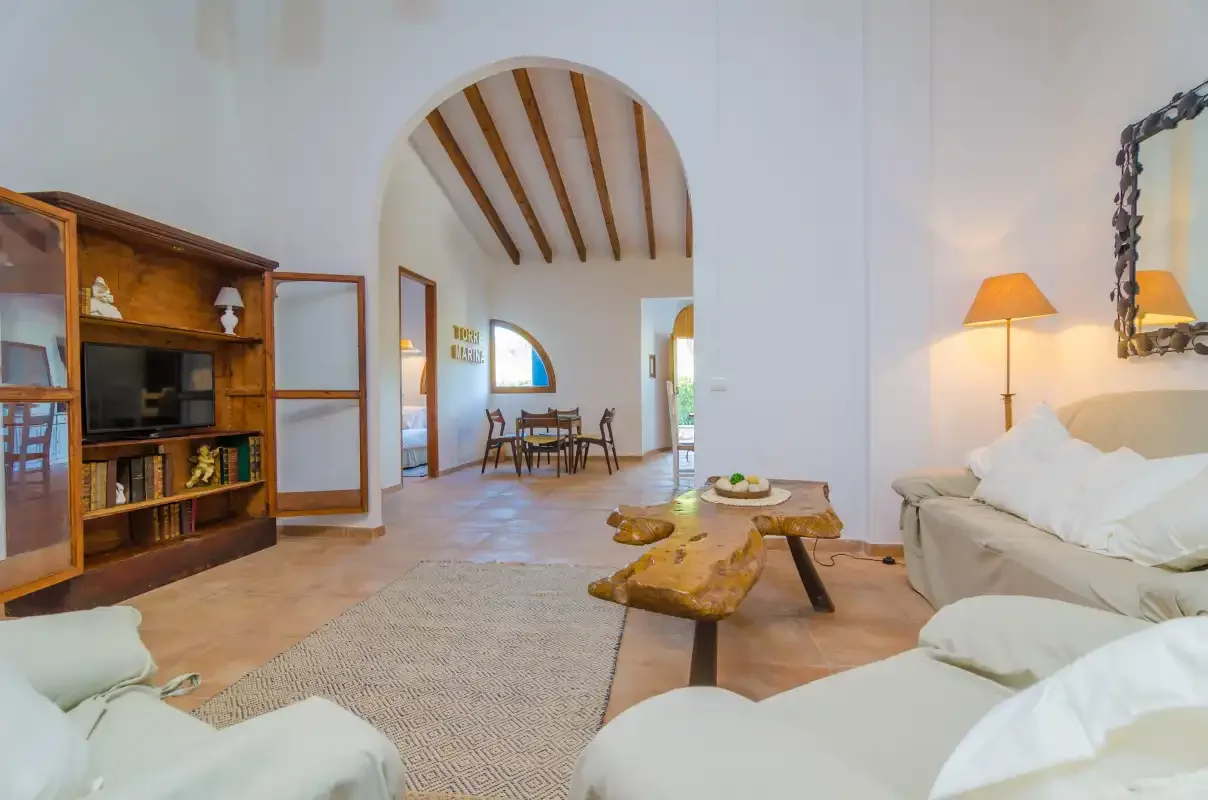 A bright living room with seating, a wooden coffee table, and an arched opening to a dining area.