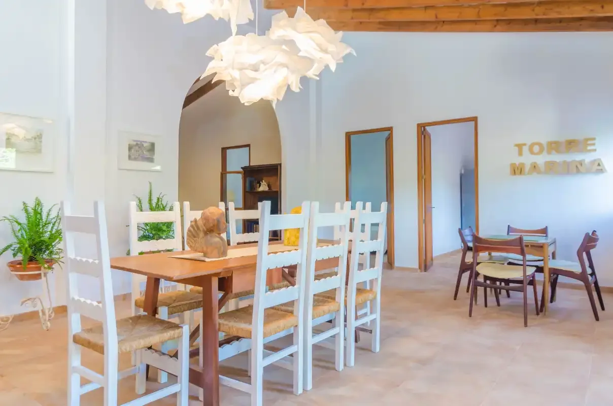 A bright dining area has a wooden table, white chairs, and pendant lights.