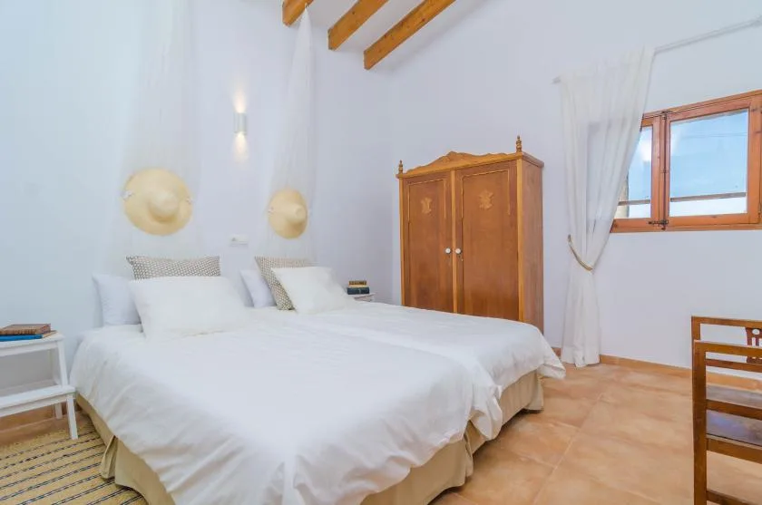 A bright bedroom with white bedding, a wooden wardrobe, and a window.