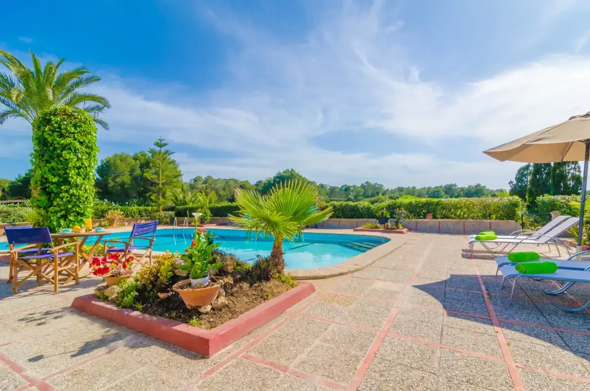 An outdoor swimming pool sits beside a paved patio with lounge chairs and greenery.