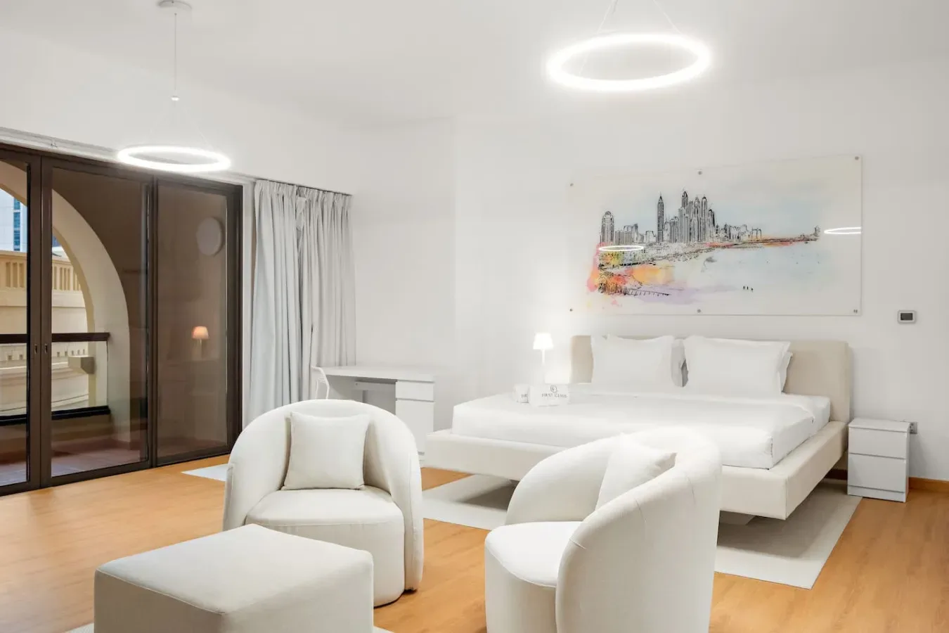 Dormitorio luminoso con una cama blanca, asientos y una gran puerta de cristal.