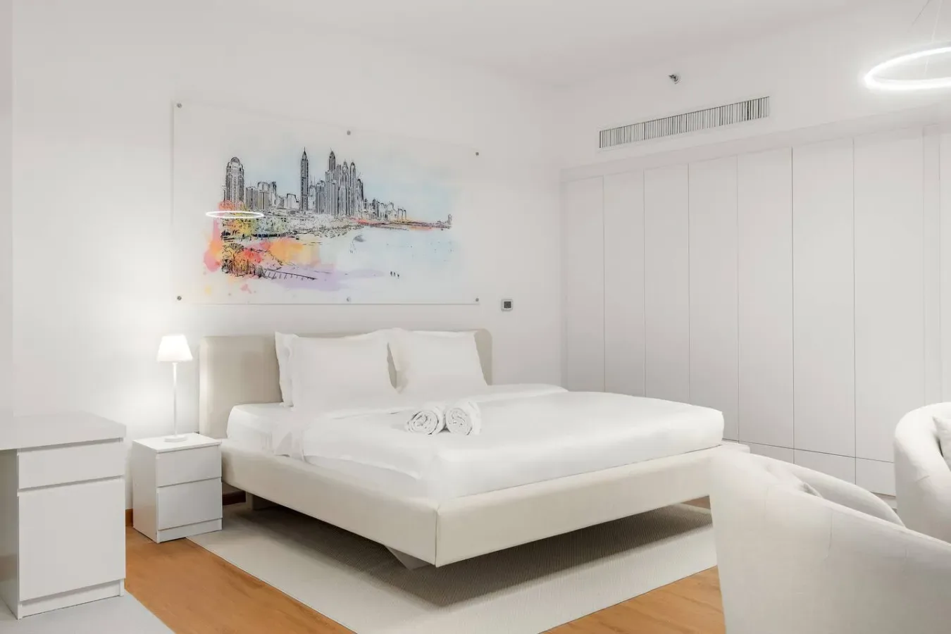 Un dormitorio luminoso con una cama blanca y una colorida ilustración urbana encima.