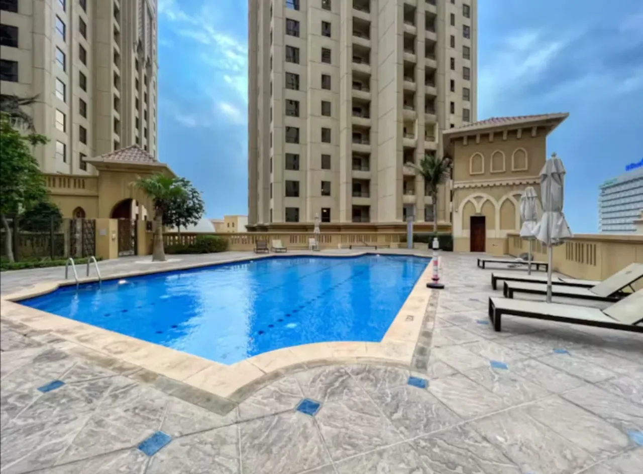 Una piscina al aire libre junto a edificios altos, con asientos de descanso en la terraza.