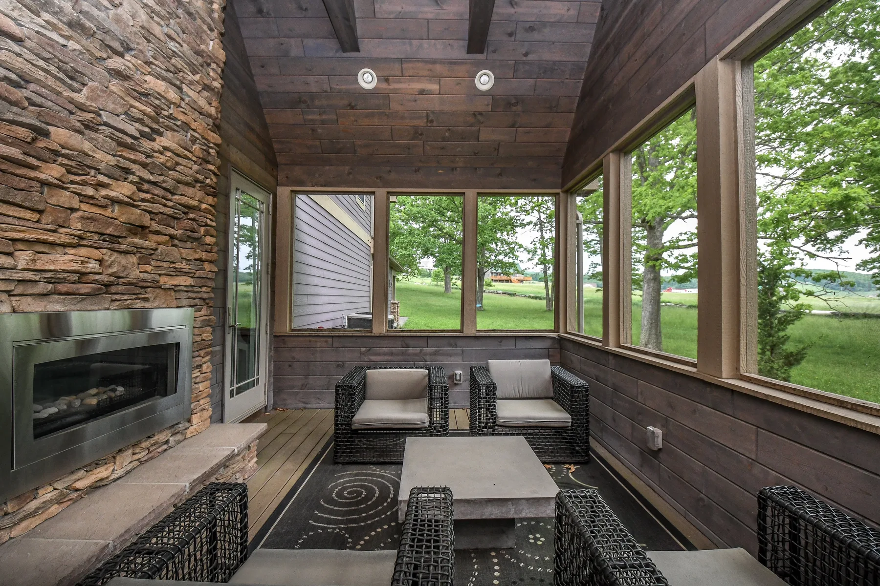 A glass-enclosed sitting area has wicker seating and a stone fireplace.