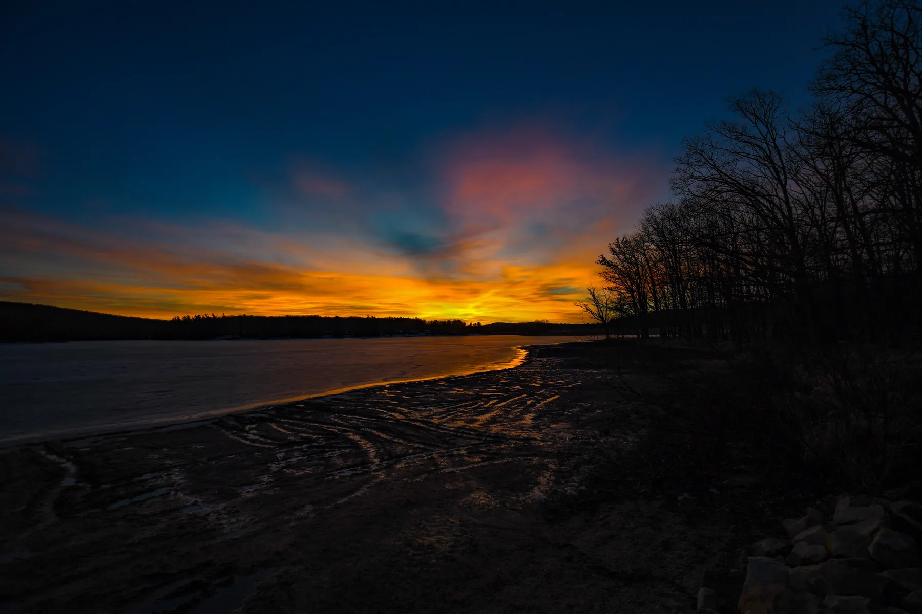 A sunset glows over a shoreline, with silhouetted trees along the water.