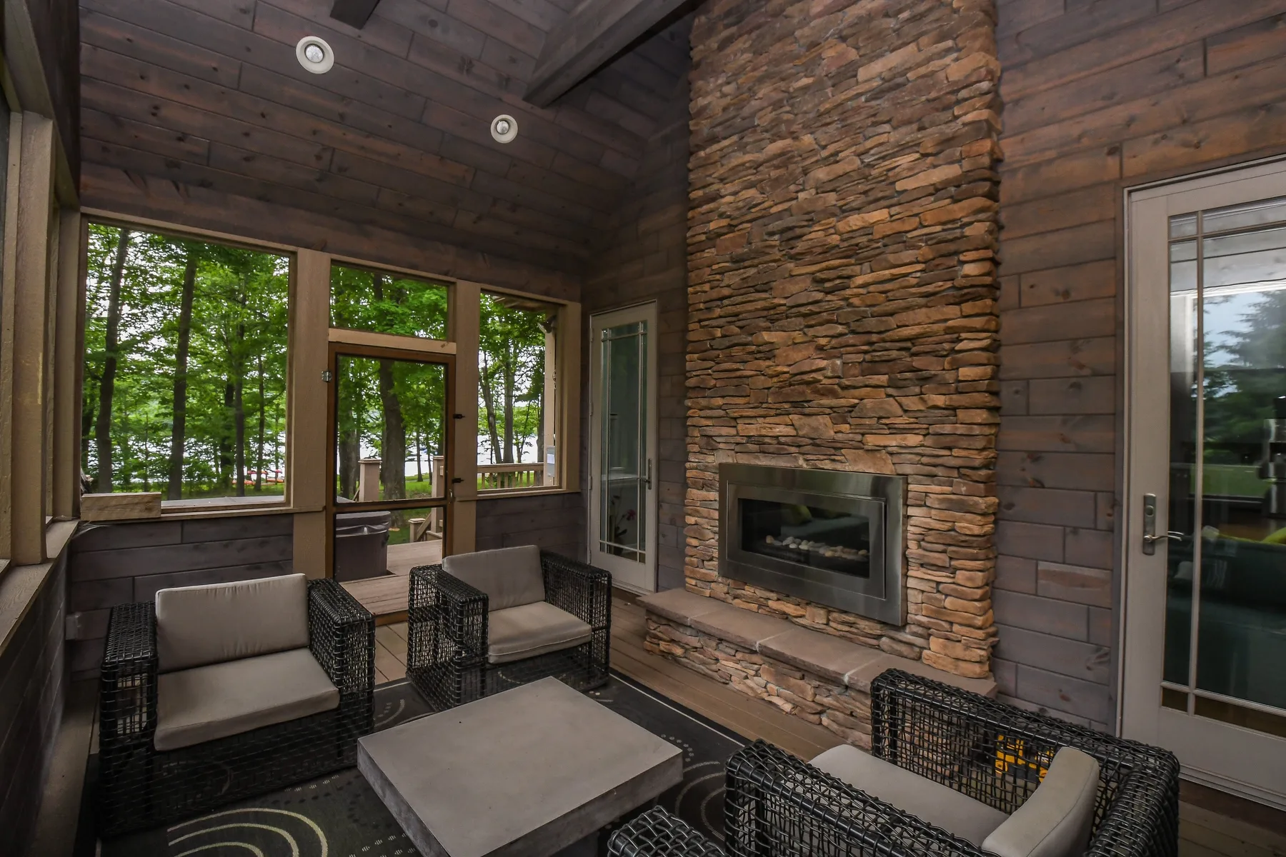 A wood-paneled living room with a stone fireplace and seating by large windows.