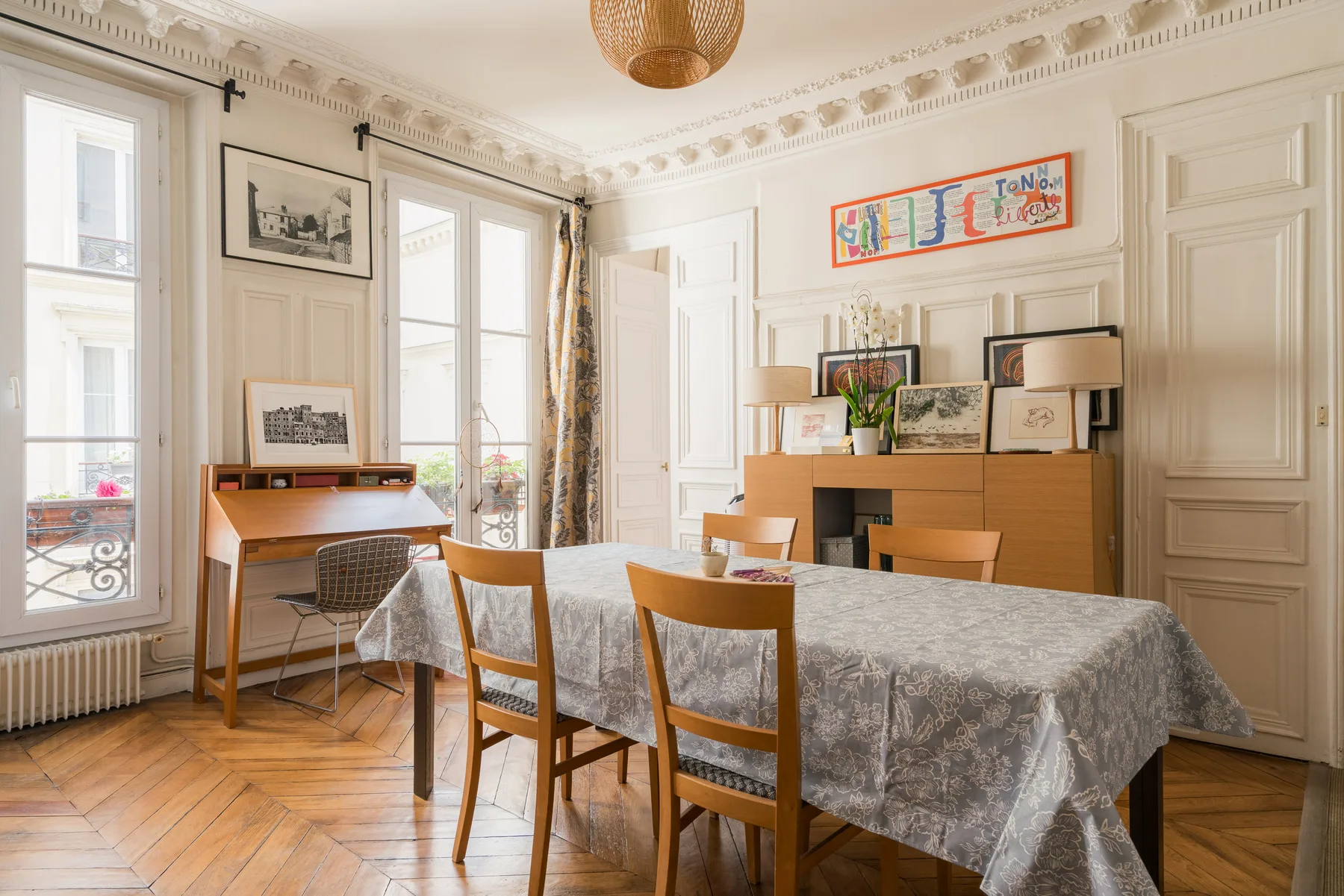A bright dining room with a long table, wooden chairs, and tall windows.