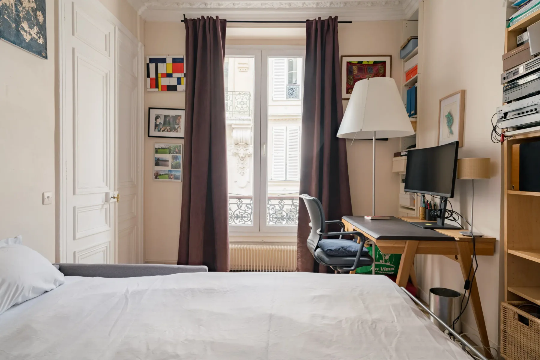 A bedroom with a bed, desk, and tall windows.