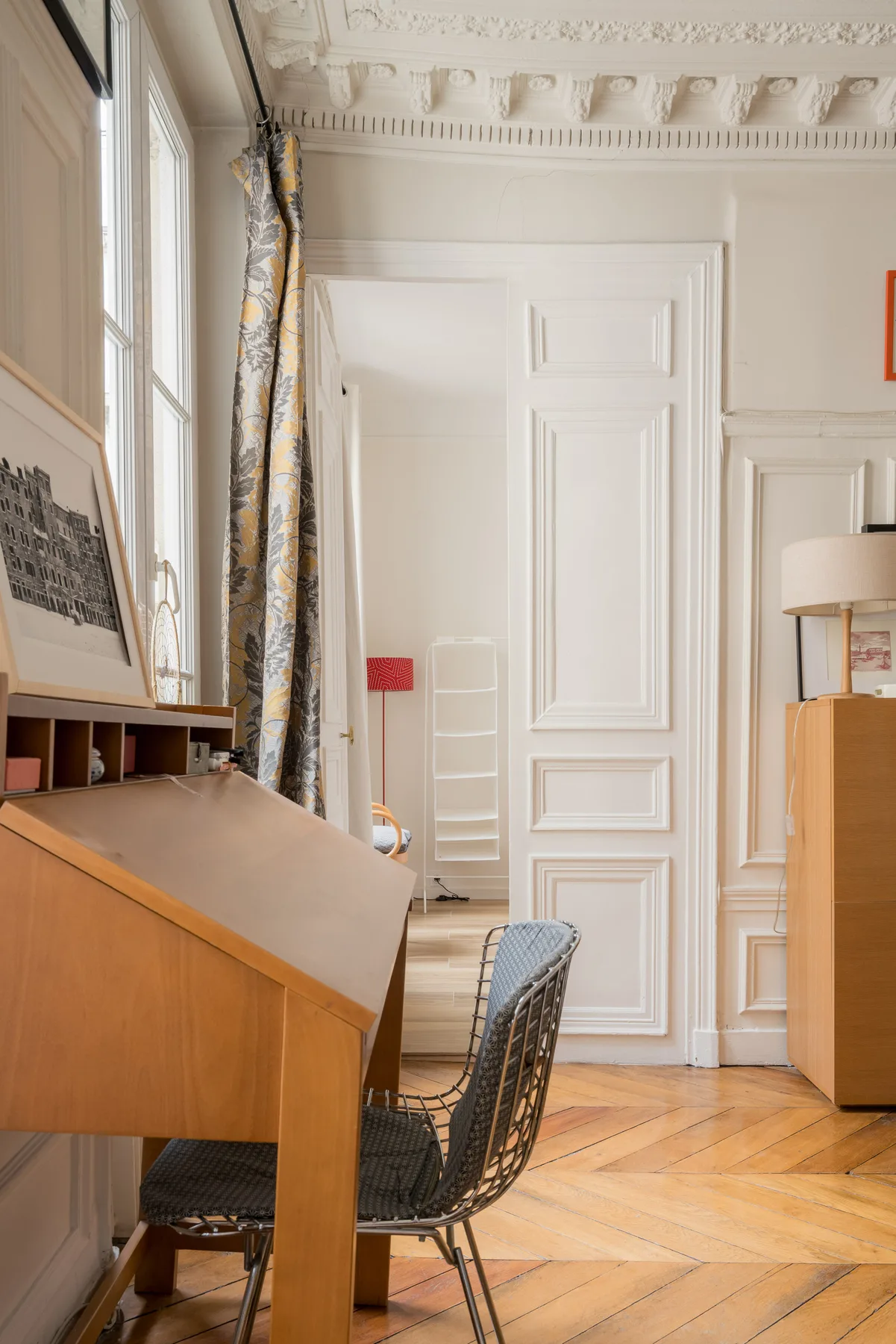 A bright room with a slanted wooden desk, a woven chair, and tall windows.