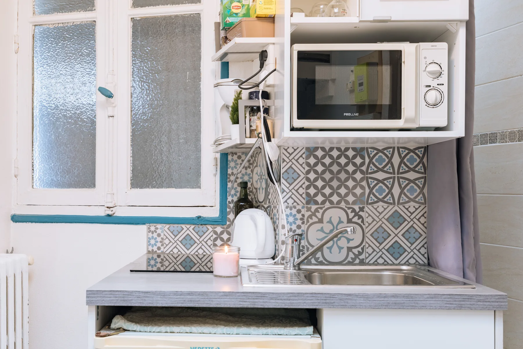 A compact kitchen counter with a sink, microwave, and patterned backsplash.
