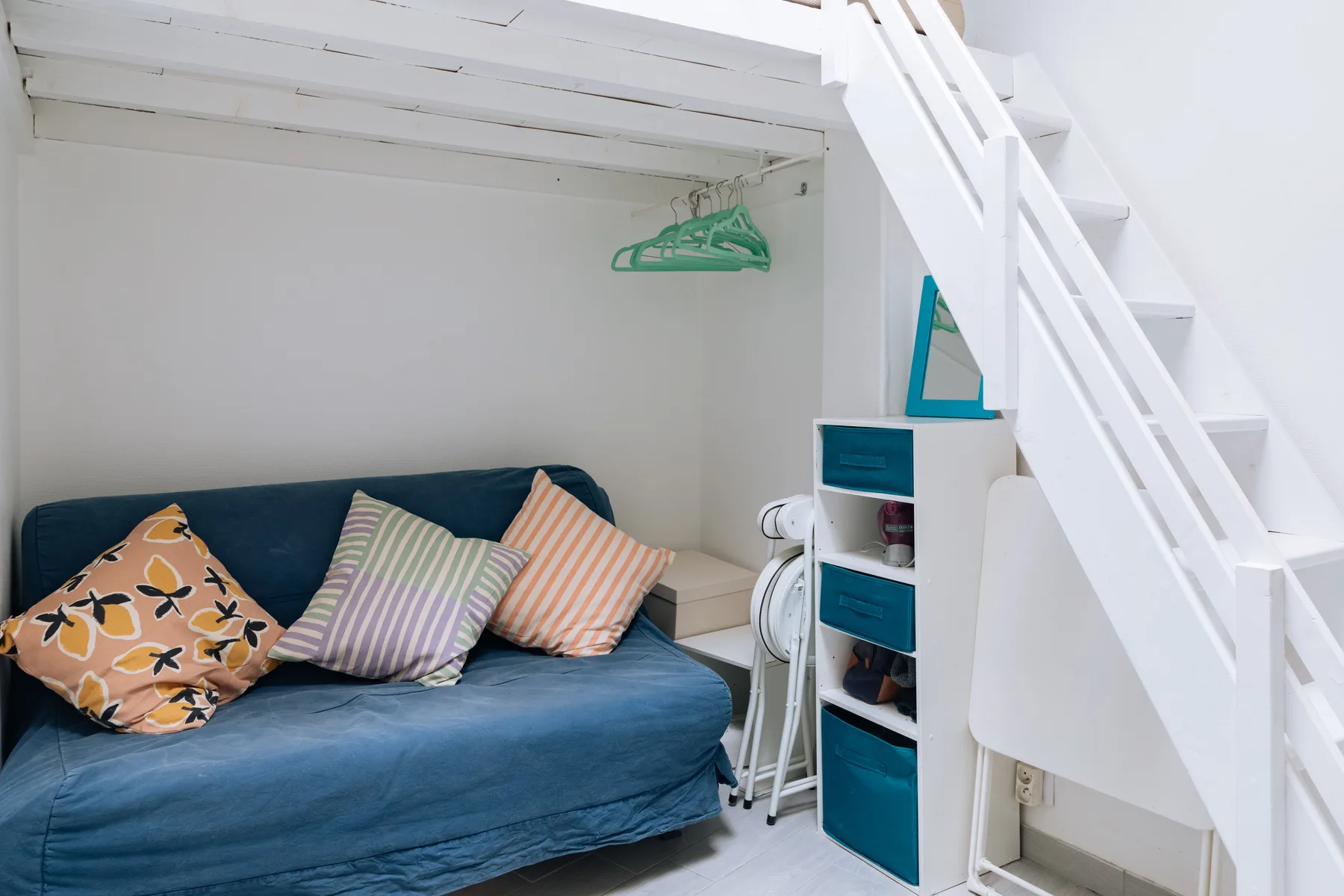 A compact sleeping area has a blue bed beneath a white loft staircase.