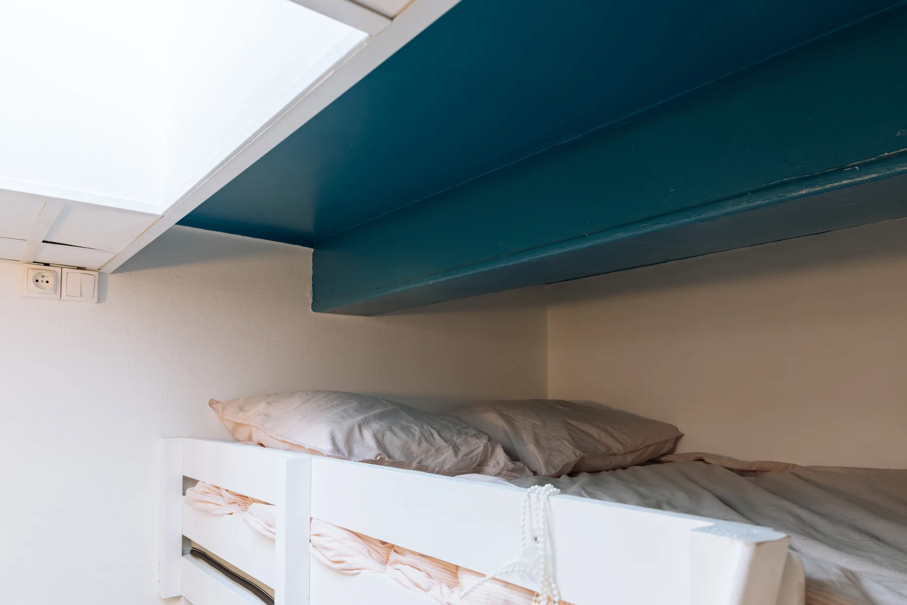 A low sleeping area with white bunk beds beneath a dark teal ceiling beam.