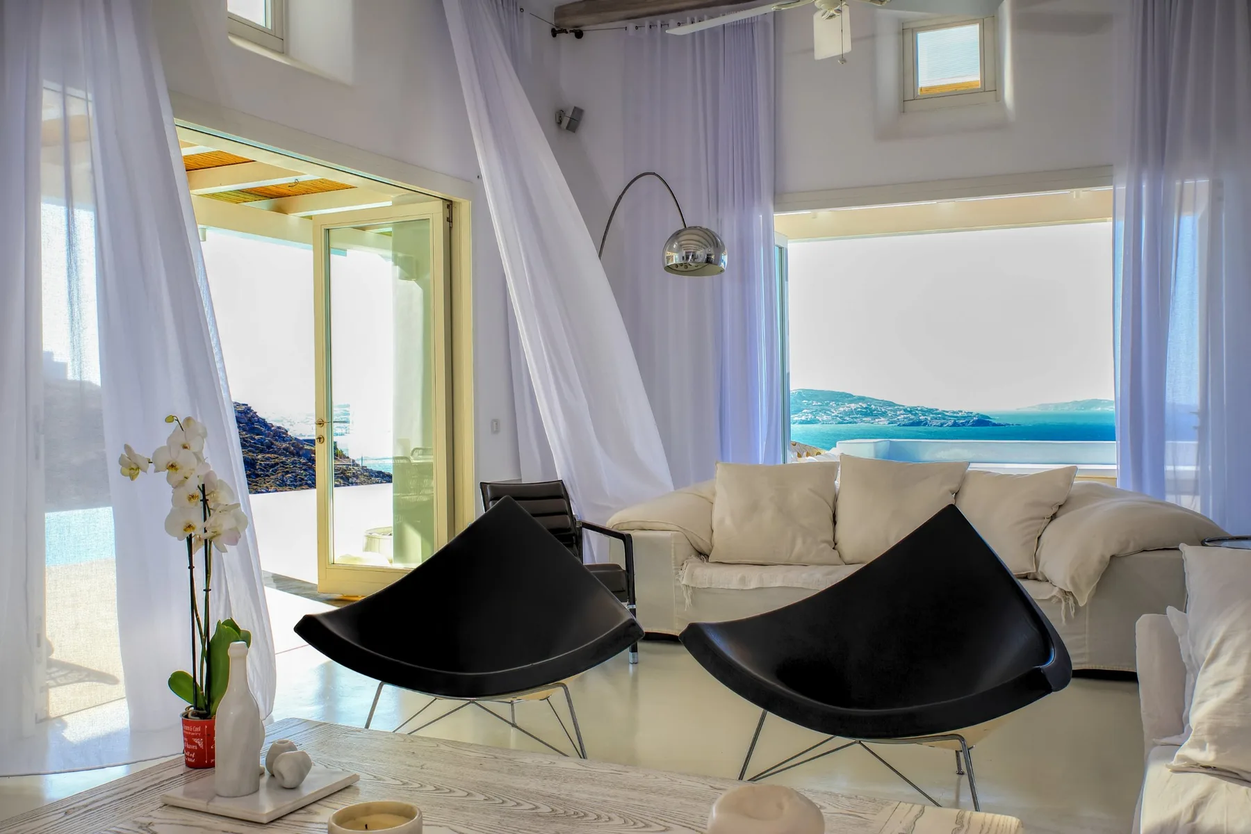 A bright living room with seating beside large windows overlooking the water.