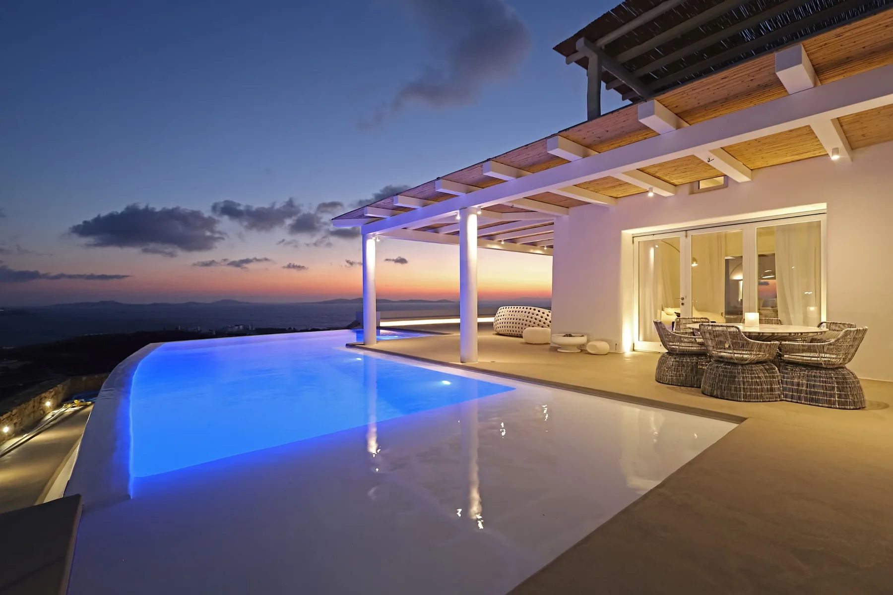 An illuminated swimming pool beside a covered patio at dusk.