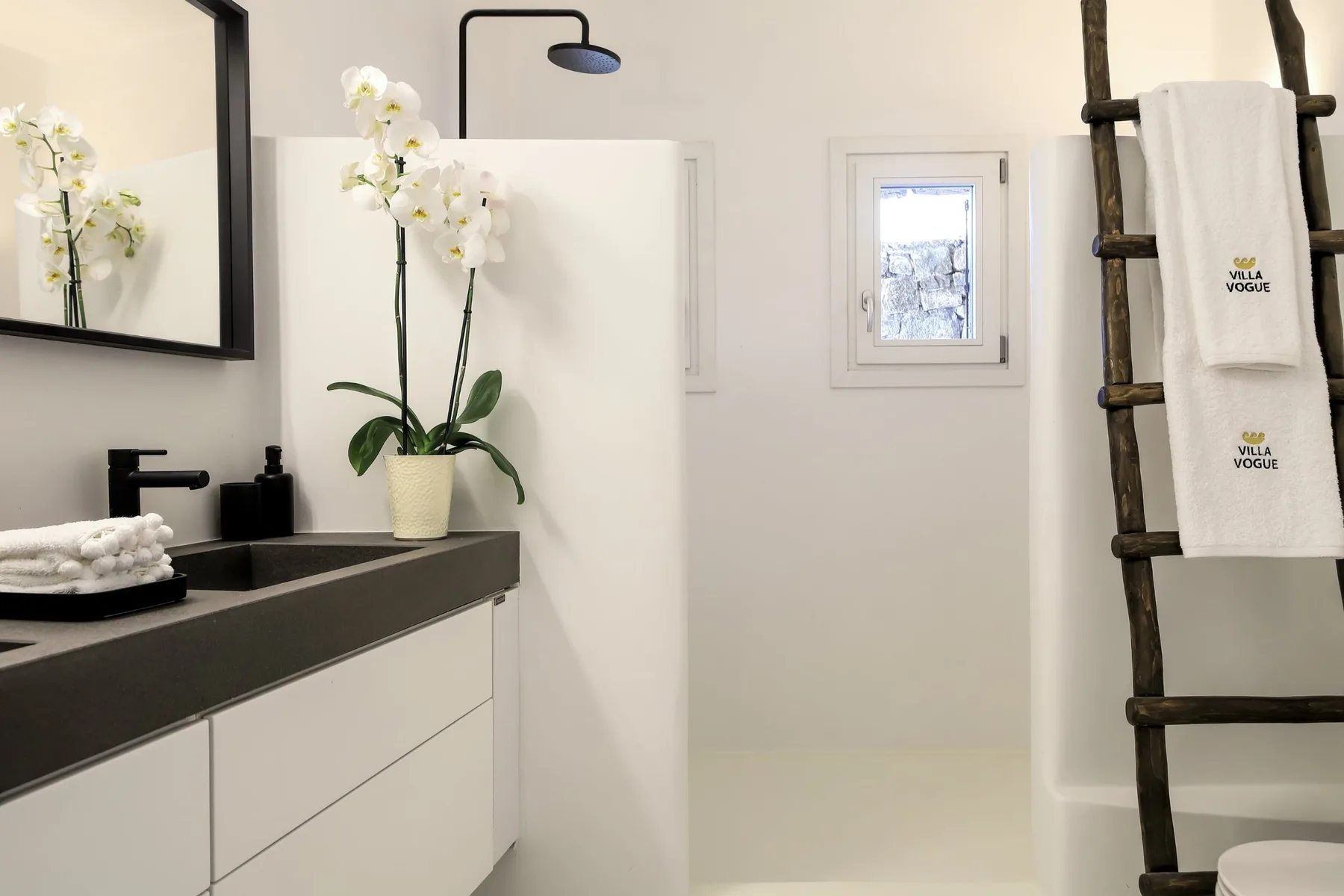 A bright bathroom with a dark vanity, white flowers, and a ladder-style towel rack.