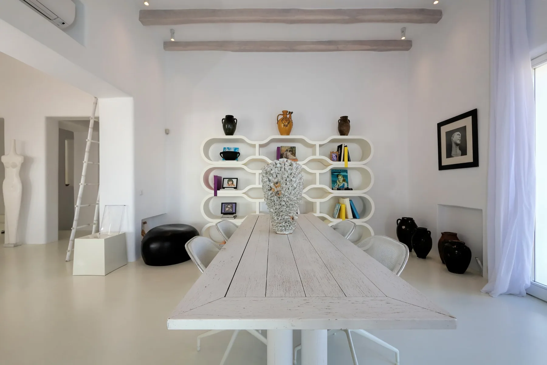 Un comedor luminoso con una mesa larga y estantes abiertos con libros y adornos.