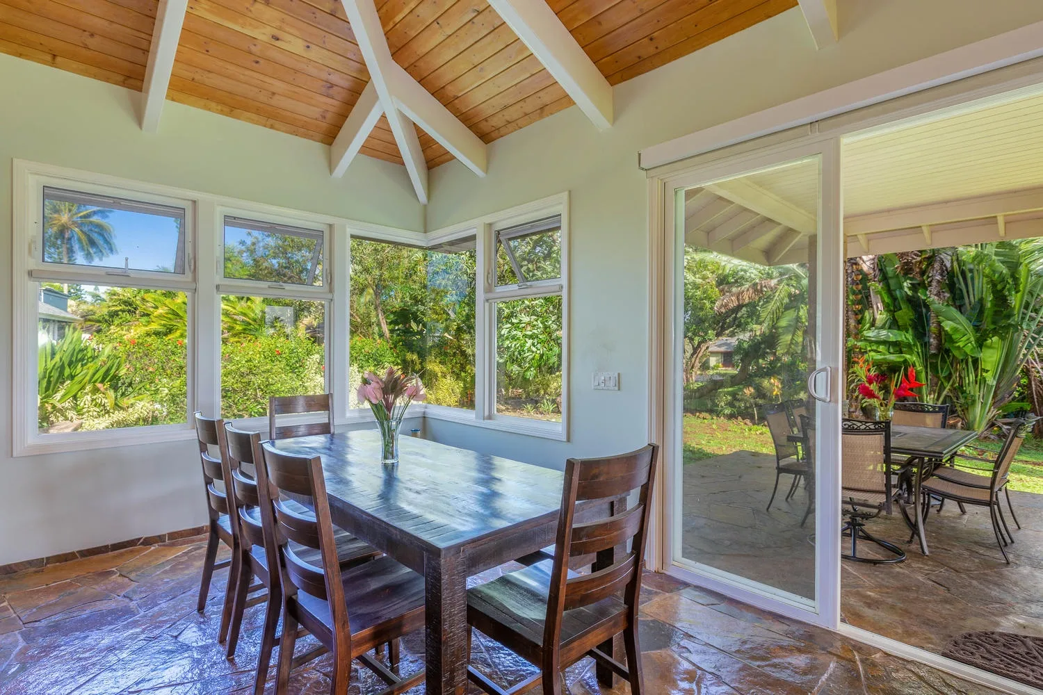 Comedor con una mesa de madera junto a grandes ventanas y una puerta de vidrio al patio.