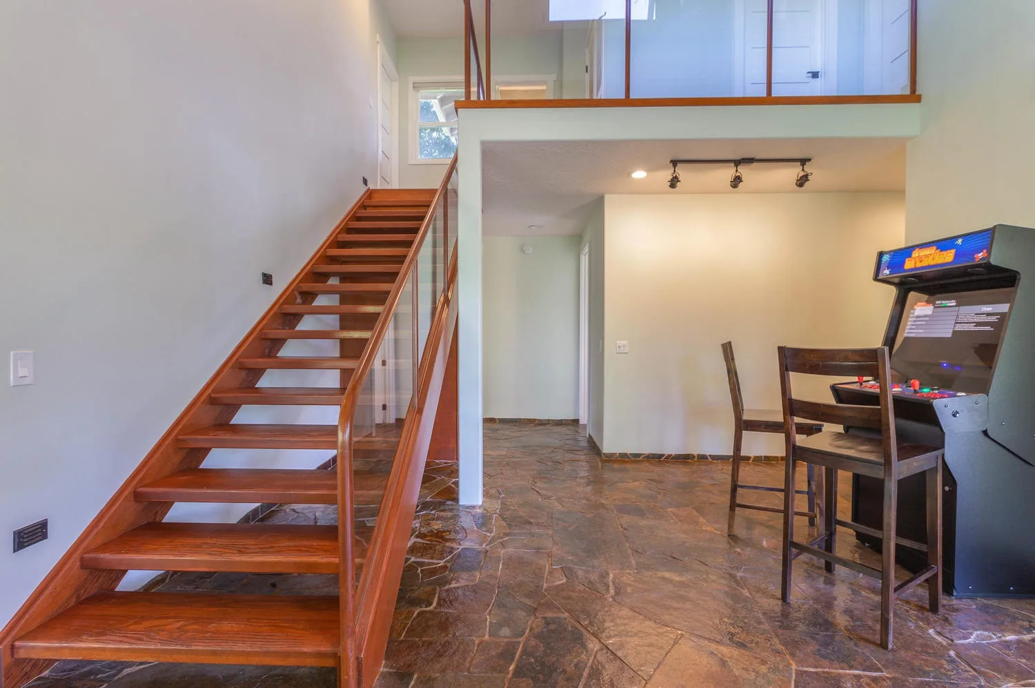 Un interior abierto con una escalera de madera, una mesa de comedor y una máquina recreativa.