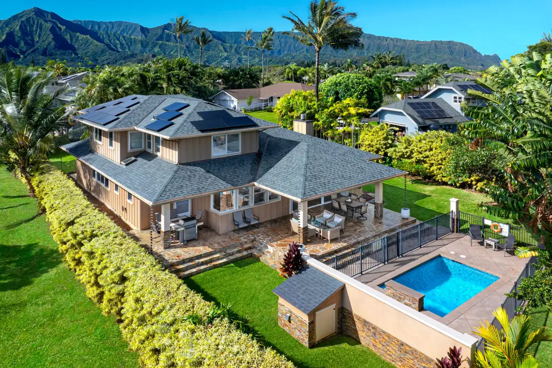Una casa grande con patio cubierto y piscina está rodeada de vegetación tropical.