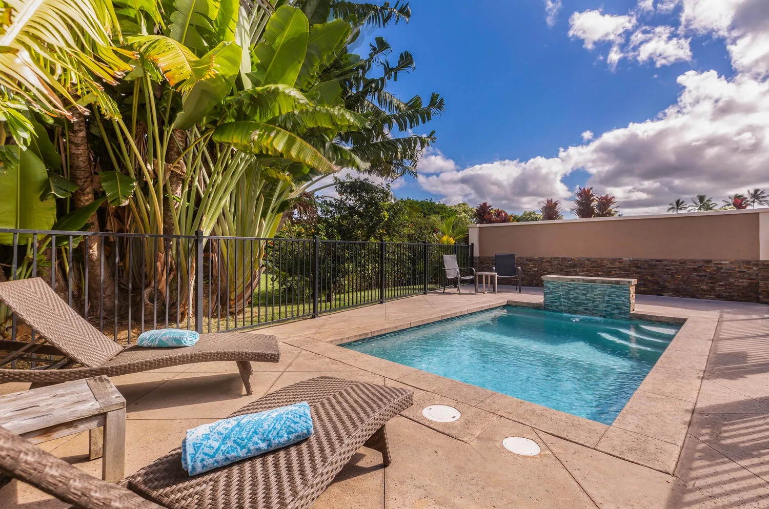 Una piscina al aire libre está rodeada por una terraza pavimentada y plantas tropicales.