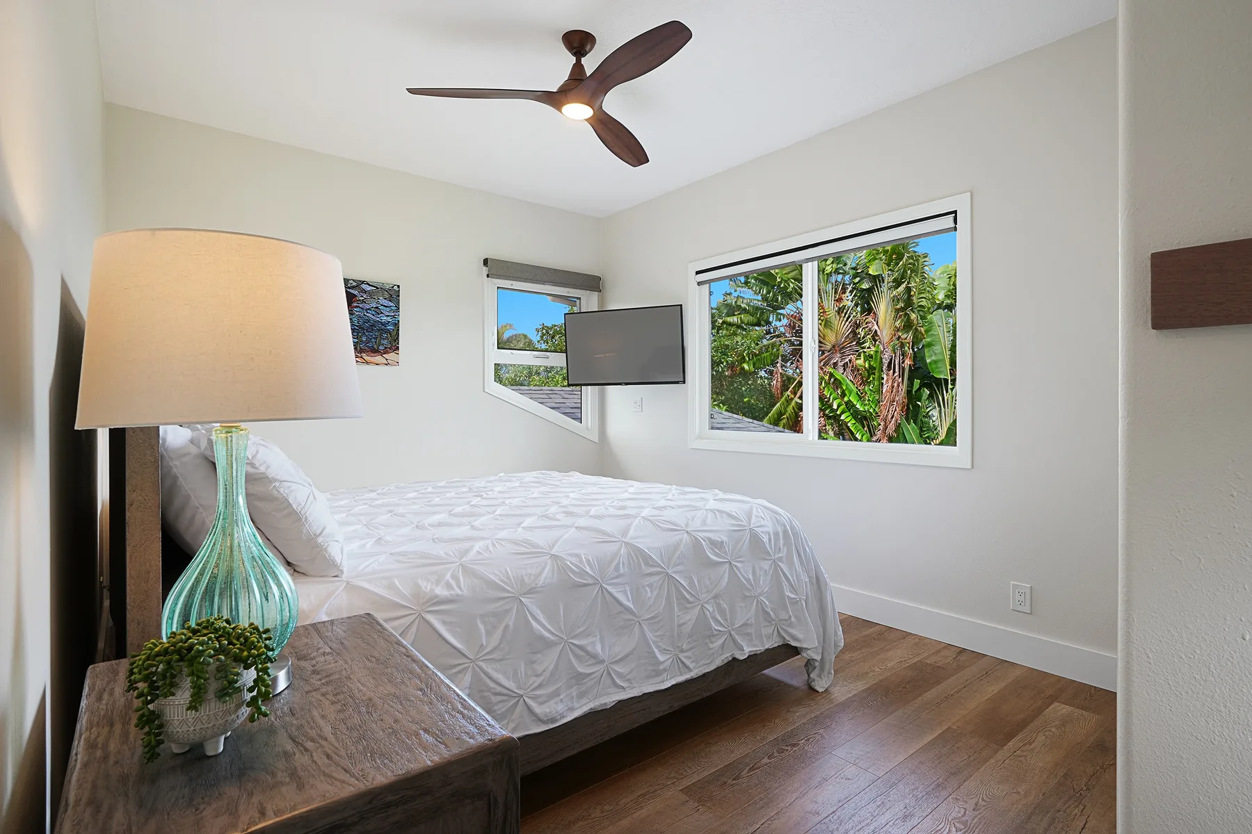 Un dormitorio con una cama bien tendida junto a ventanas con vistas a la vegetación.