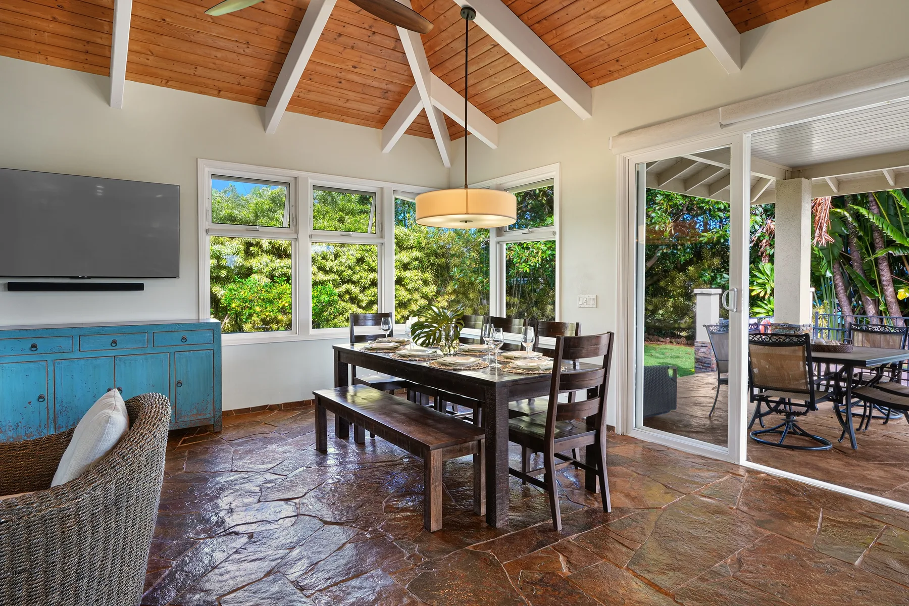 Comedor con una mesa de madera junto a grandes ventanas y puertas corredizas de vidrio.