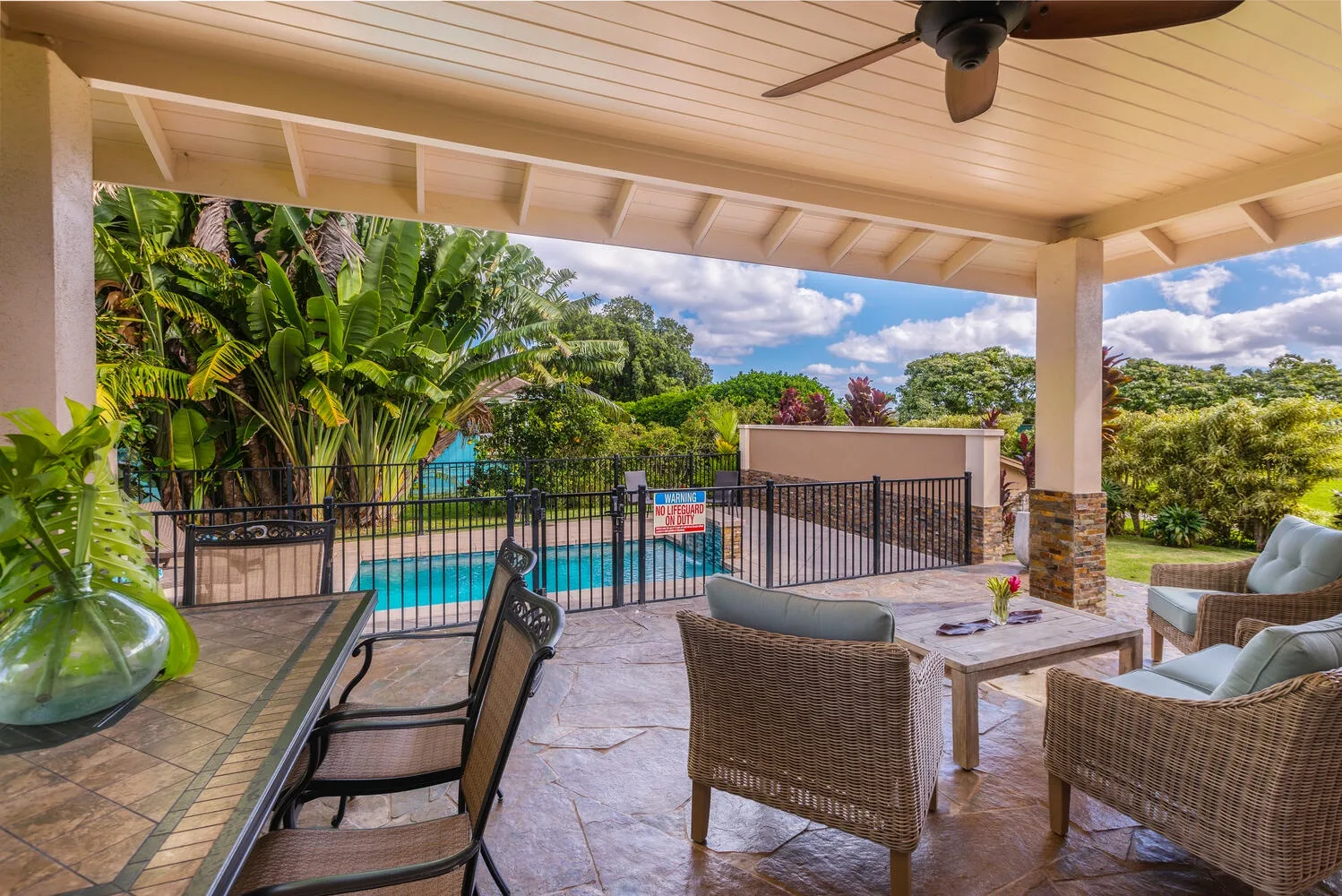 Un patio cubierto con asientos al aire libre da a una piscina y una vegetación frondosa.
