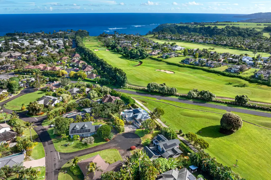 Vista aérea de un barrio residencial junto a un campo de golf verde, con el océano al fondo.