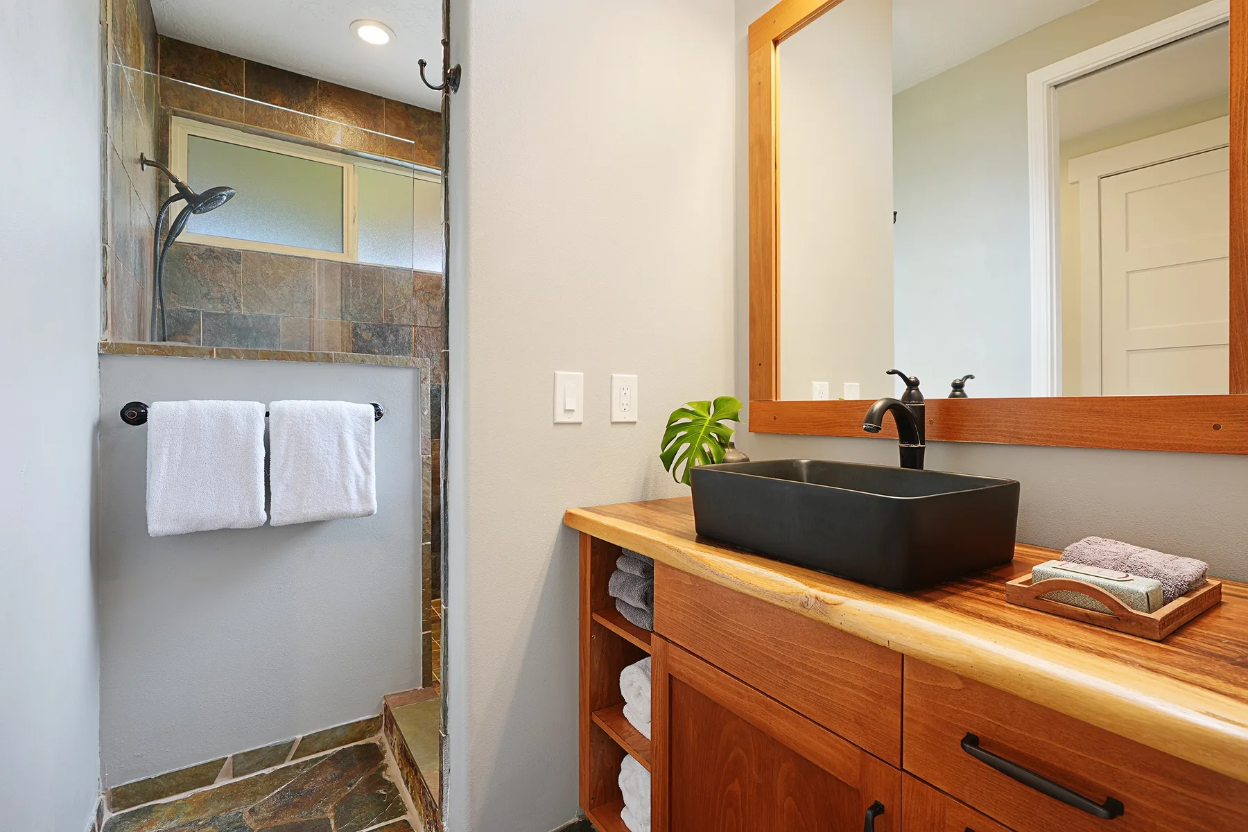 Un mueble de baño con lavabo negro está junto a una ducha con azulejos.