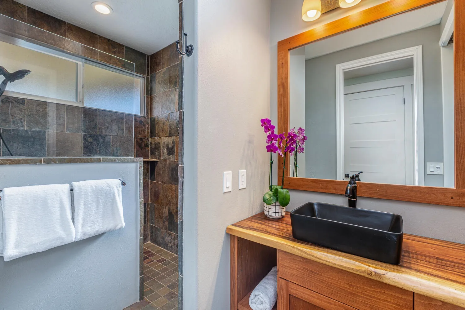 Un baño con una ducha de vidrio y un mueble de madera con lavabo negro.