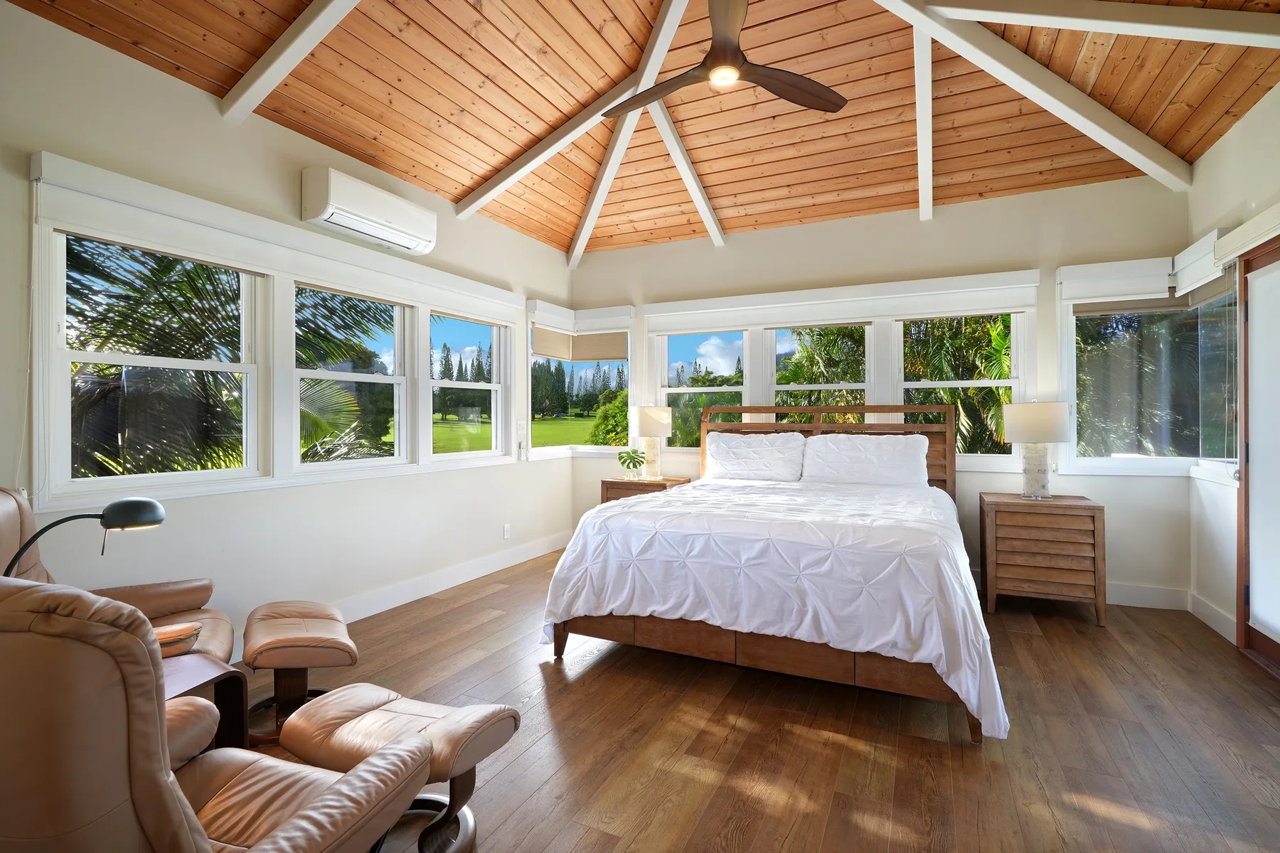 Un dormitorio luminoso con una cama bajo un techo abovedado de madera y ventanas alrededor.