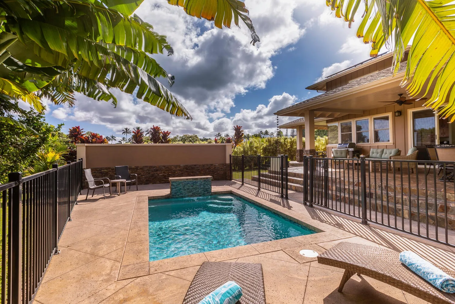 Una piscina está en un patio soleado junto a una casa y asientos al aire libre.