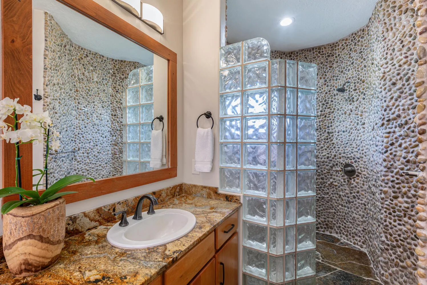Un baño con lavabo, espejo y una mampara de bloques de vidrio.