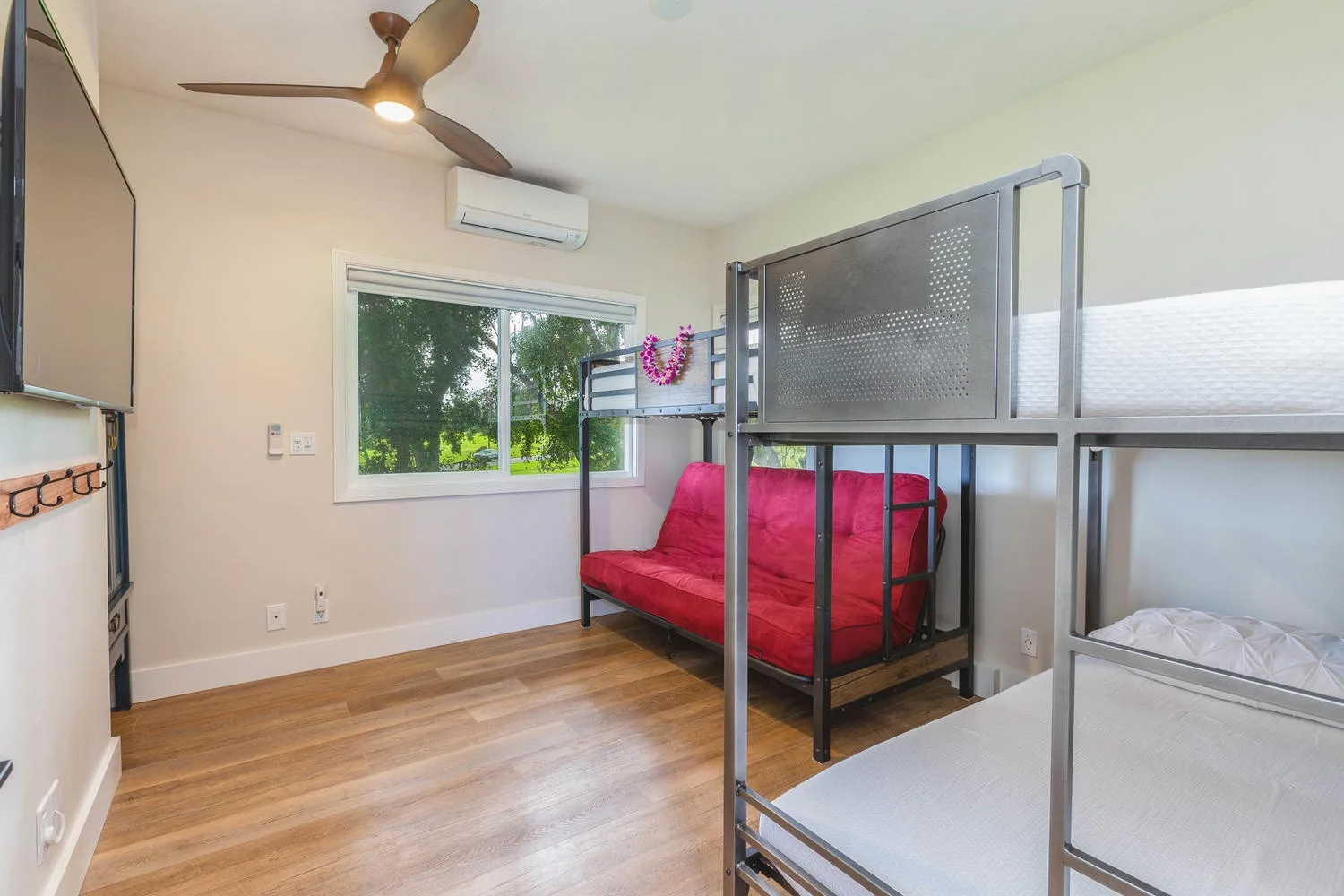 Un dormitorio con literas, un sofá rojo y una ventana con vista a la vegetación.