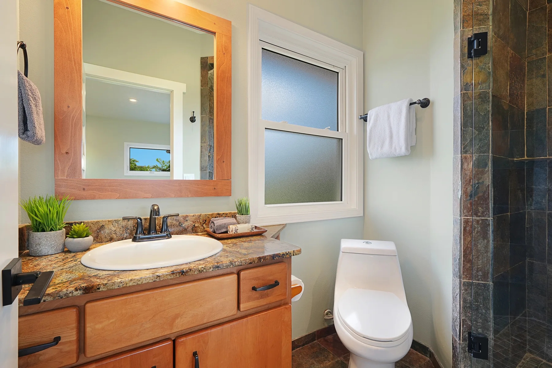 Un baño con tocador de madera, ventana esmerilada, inodoro y ducha revestida de azulejos.