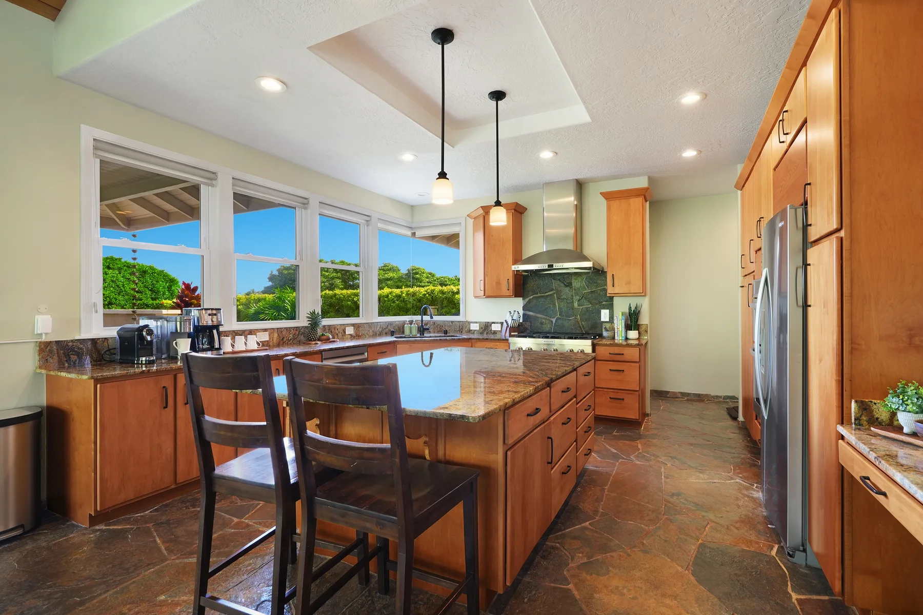 Una cocina amplia con isla central, gabinetes de madera y ventanas grandes.