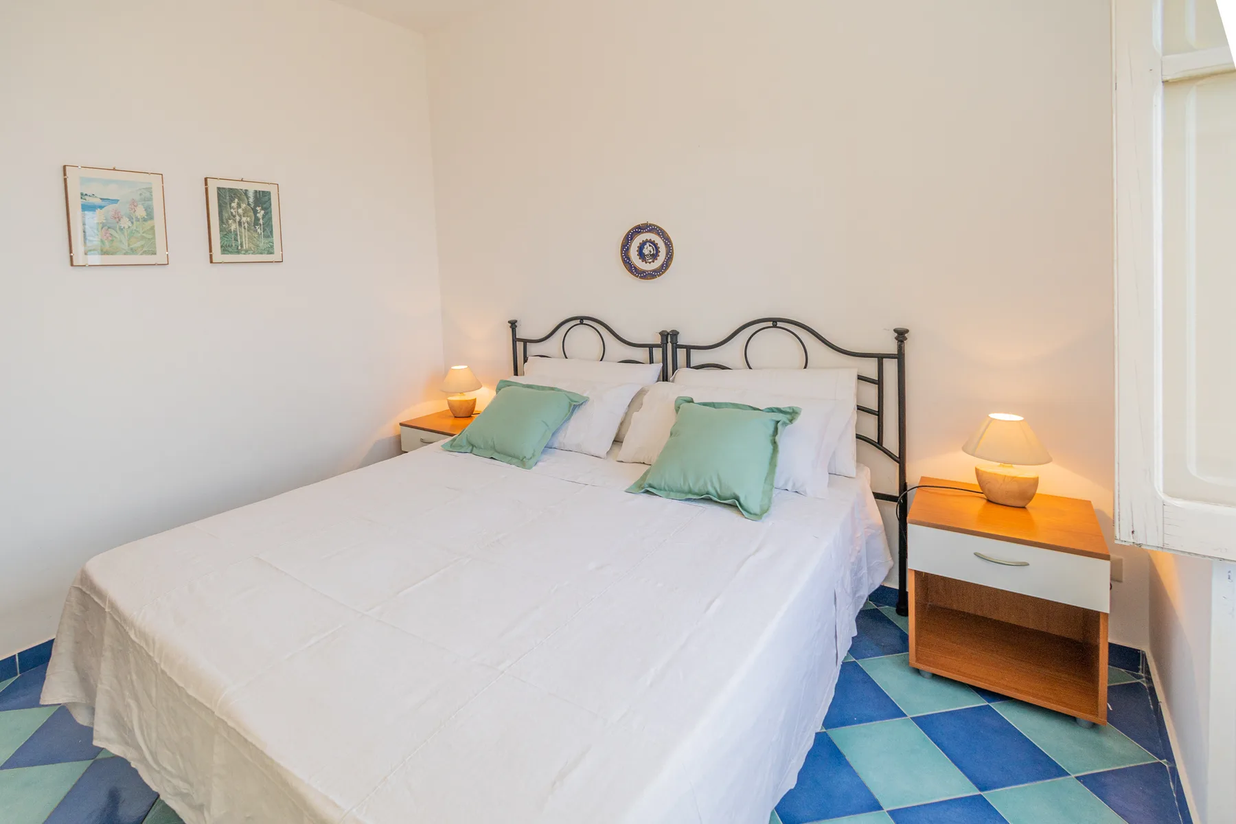 A bedroom with a large bed, bedside tables, and blue patterned flooring.