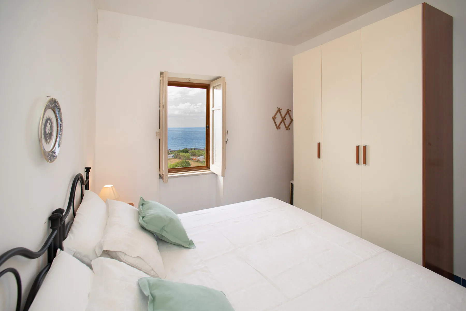 A bedroom with a bed, a wardrobe, and an open window overlooking the sea.