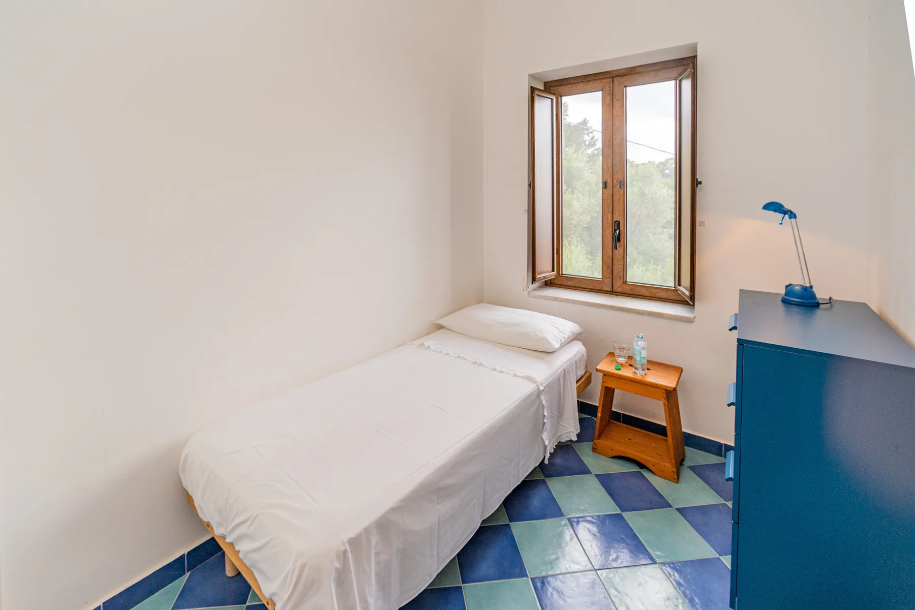 A bright bedroom with a single bed beside a wooden-framed window.