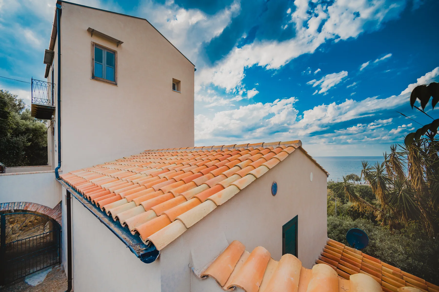 A seaside house with pale walls and terracotta roof tiles beneath a blue sky.