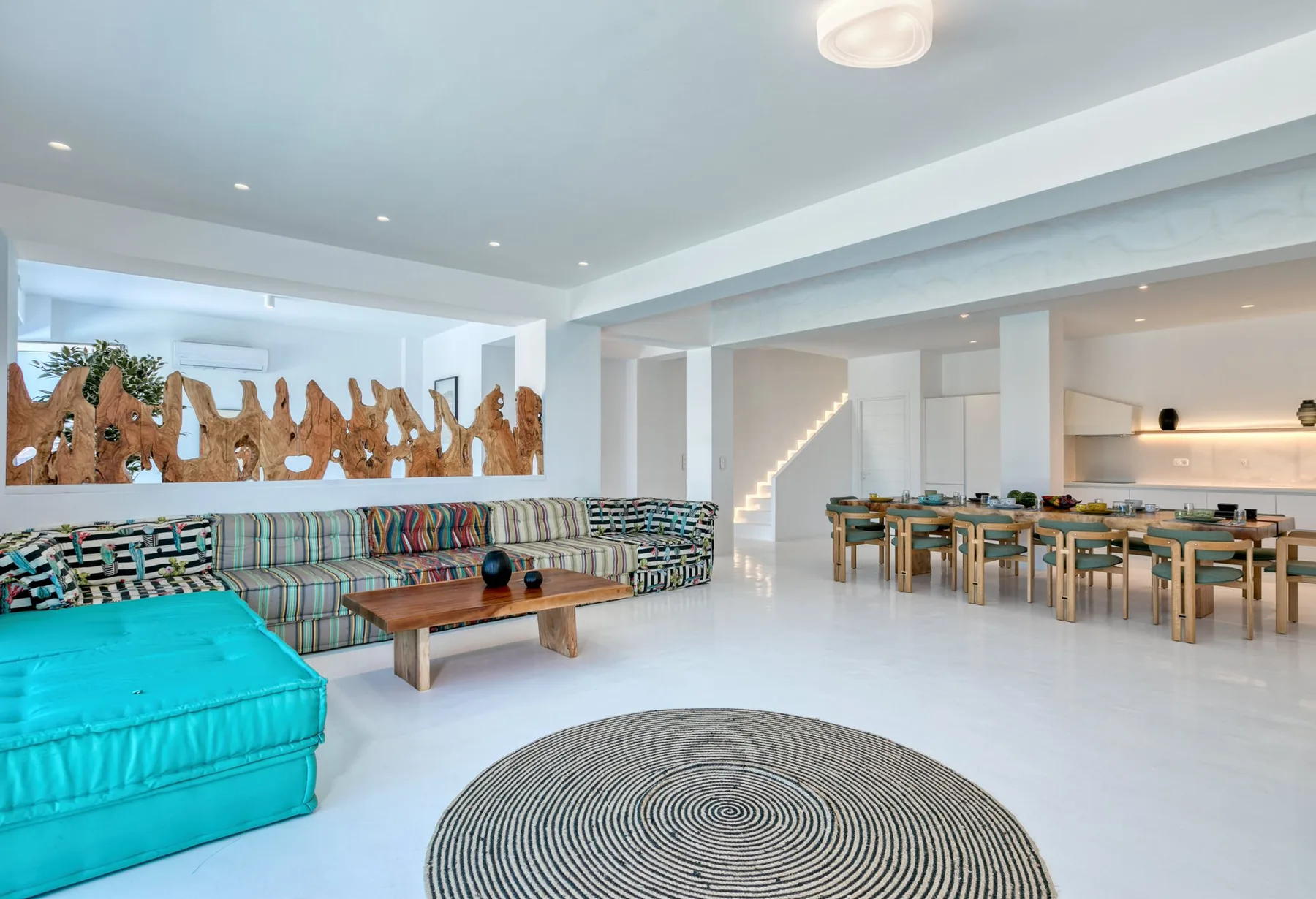 A bright open-plan living and dining area with colorful seating and a long table.